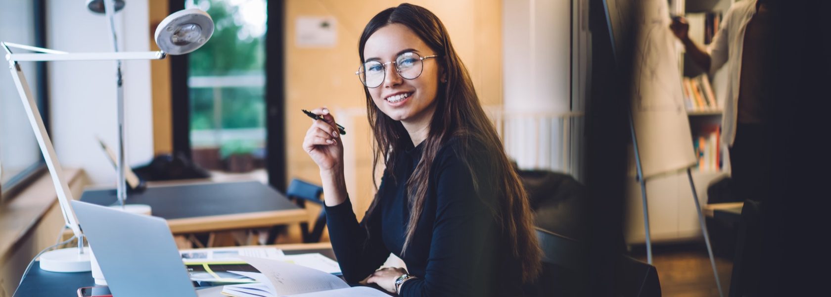 A smiling student at a desk with a laptop during a live online class
