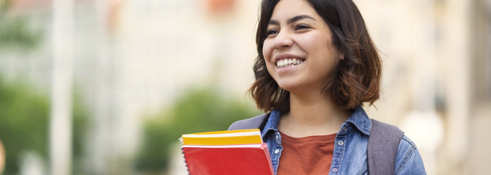 A smiling student holding notebooks outdoors