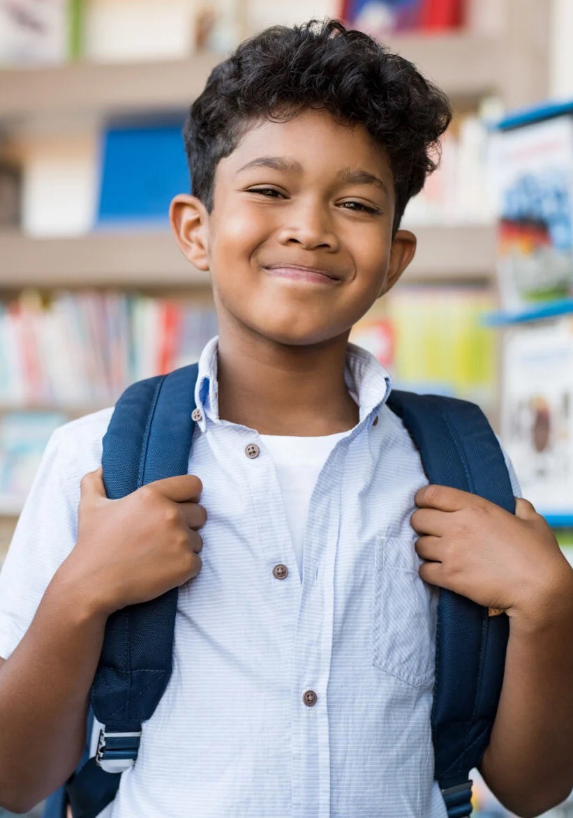 A smiling student with a backpack standing in a library