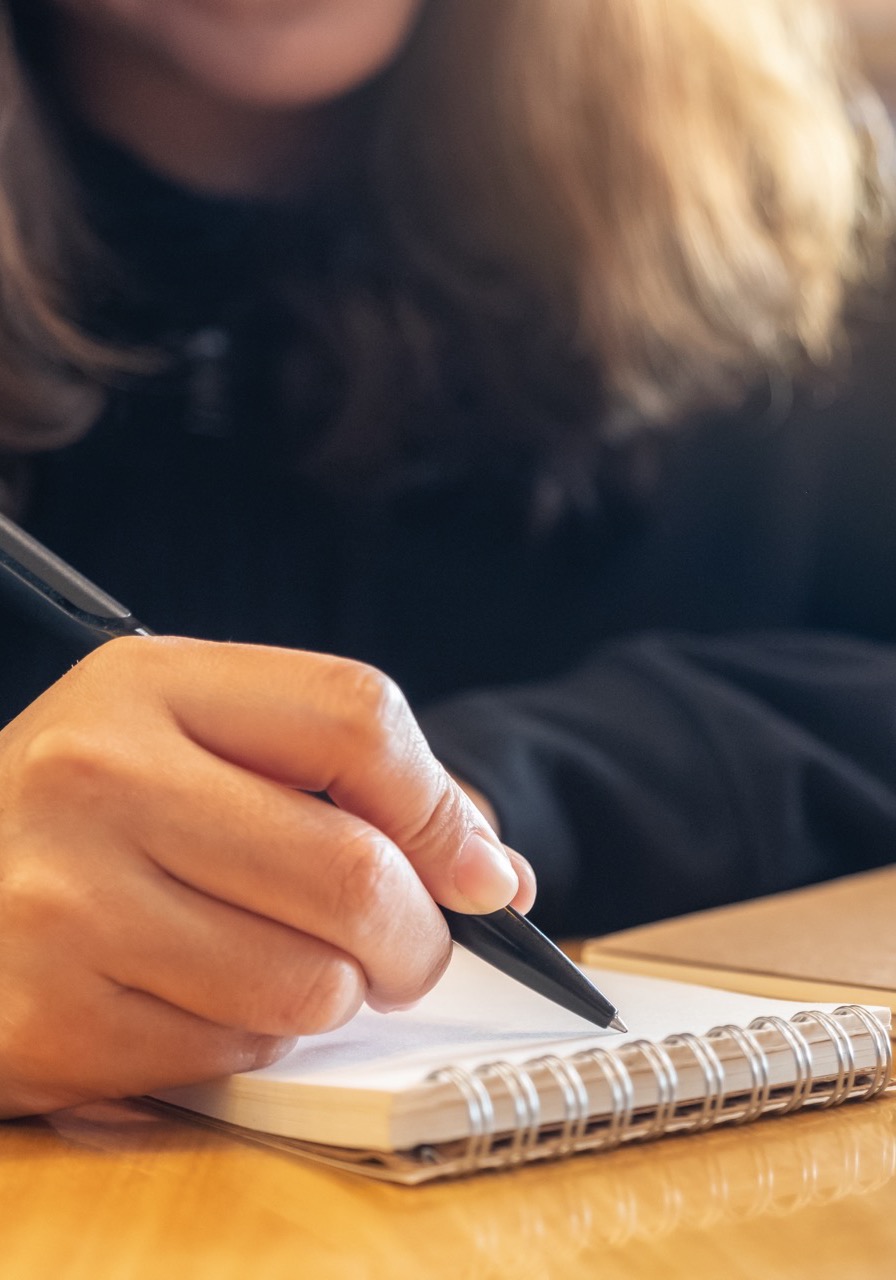 A student taking notes by hand in a spiral notebook