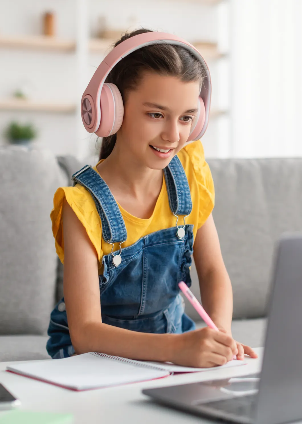 Homeschool student in headphones taking notes during a live online class on her laptop