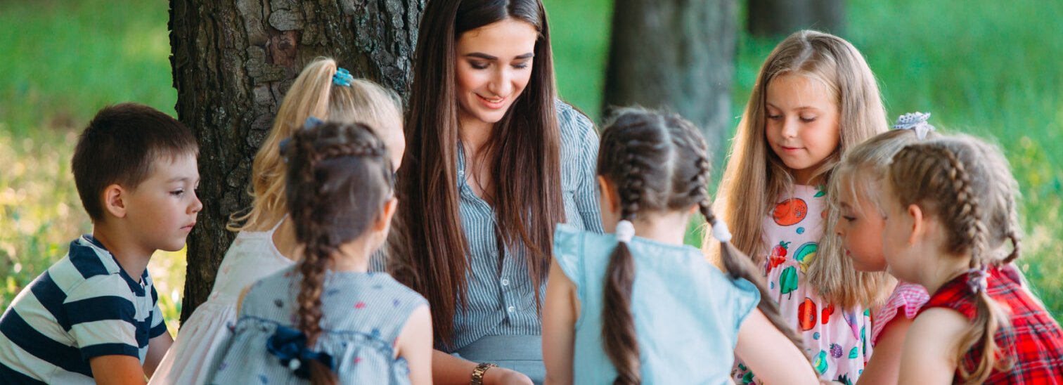 A teacher reading to a circle of children under a tree
