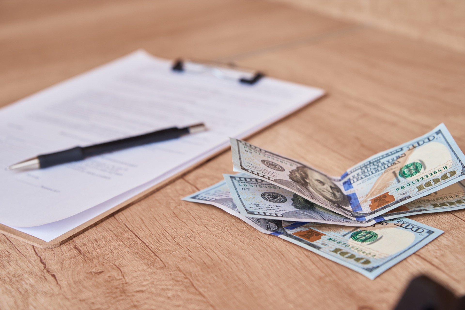 Paperwork, a pen, and dollar bills on a wooden table