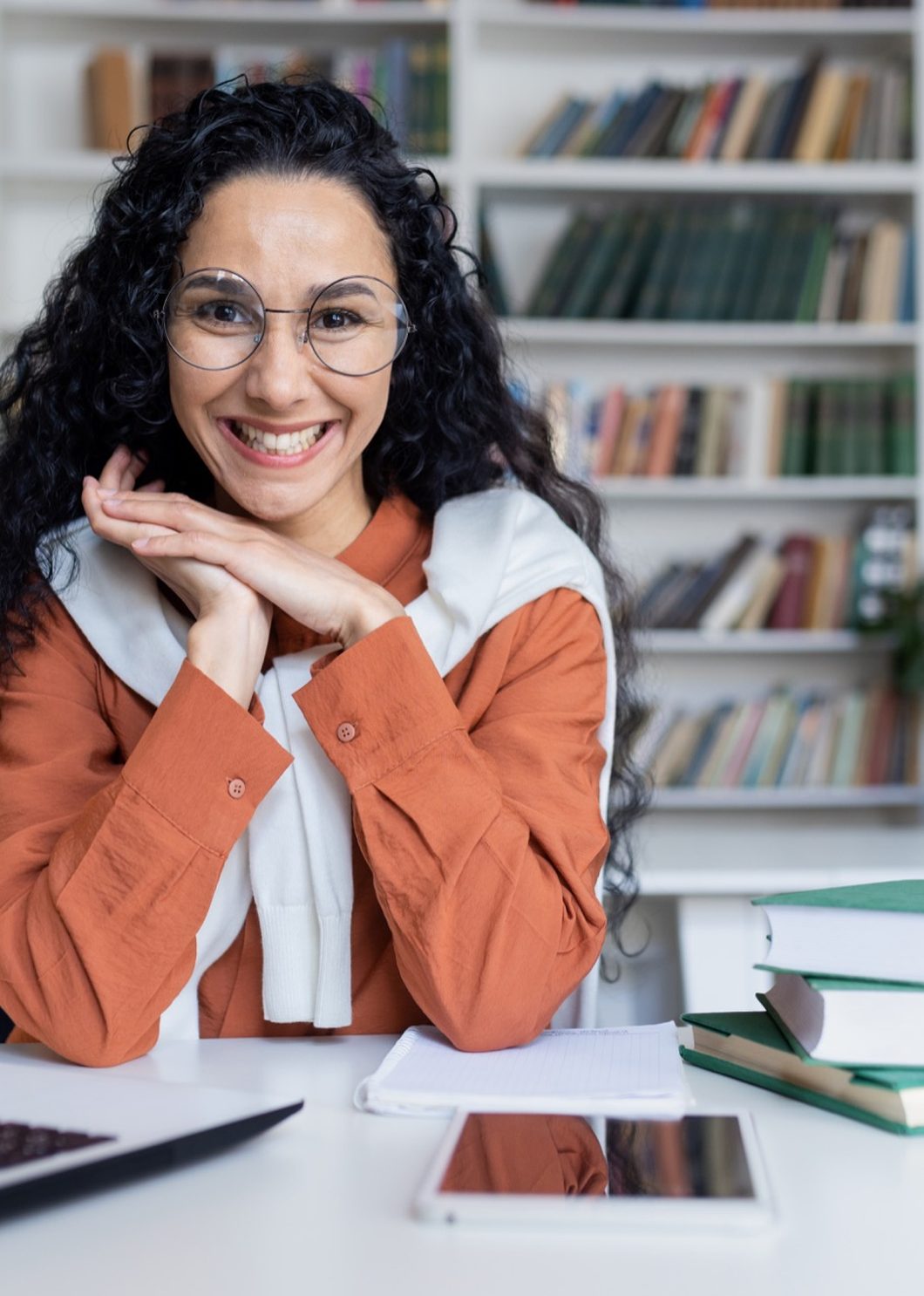 A smiling instructor in glasses seated at a laptop in front of bookshelves