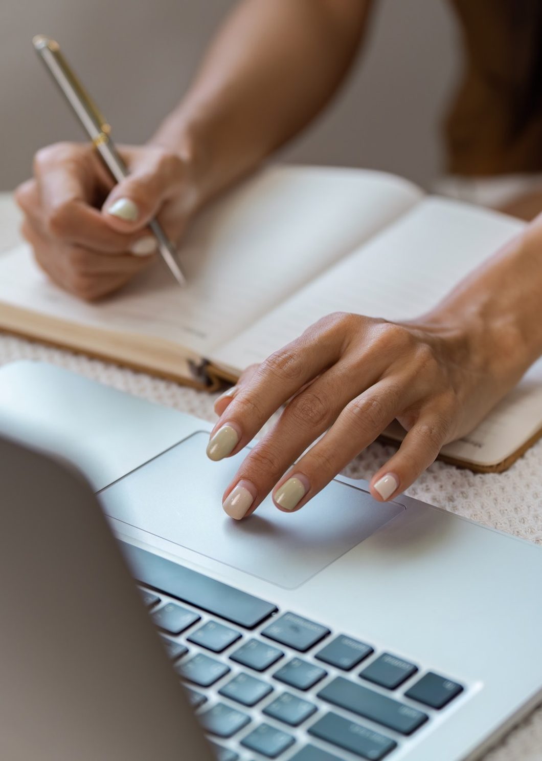 Hands writing in a notebook beside a laptop