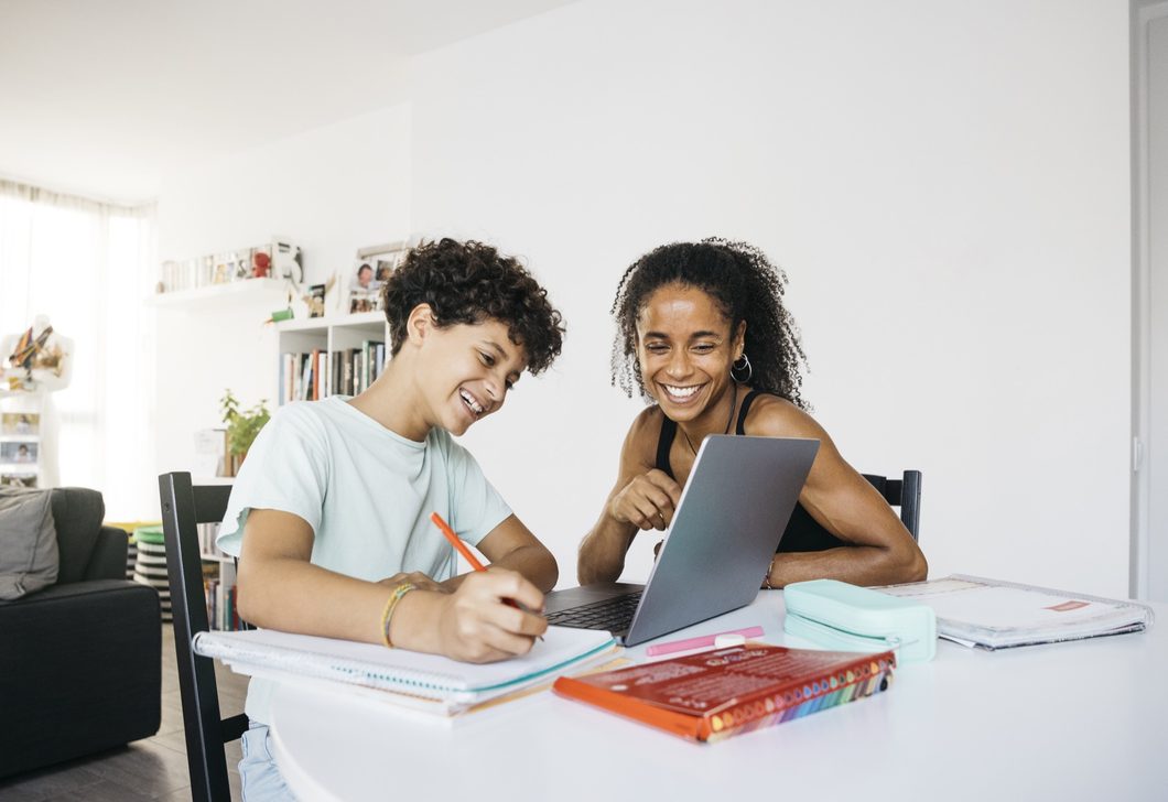 A mother and daughter laughing while studying online with a laptop at home