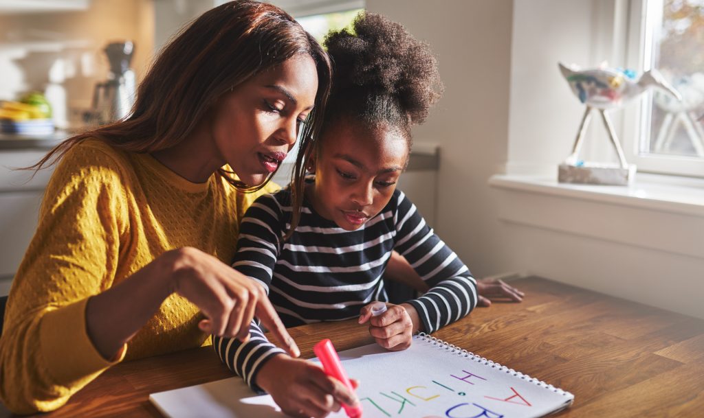 A mother and young daughter working through a lesson together at the kitchen table