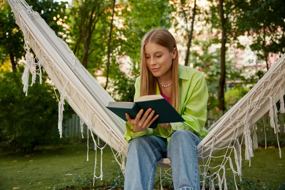 Teenage girl reading a green hardcover in a garden hammock, working through an 8th grade summer reading list