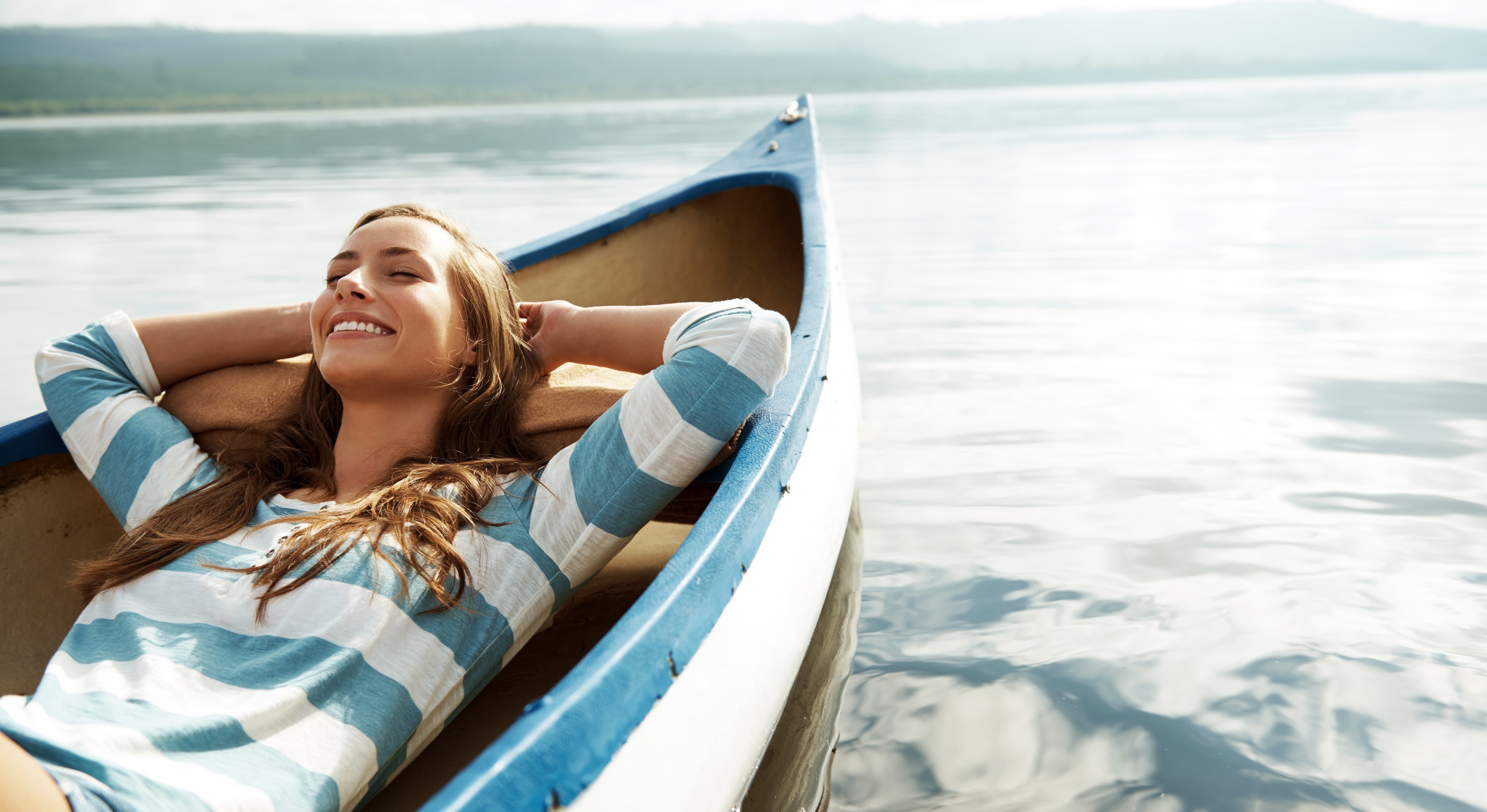 Young woman lying back in a canoe on calm water, a restful start to a summer reading list by grade