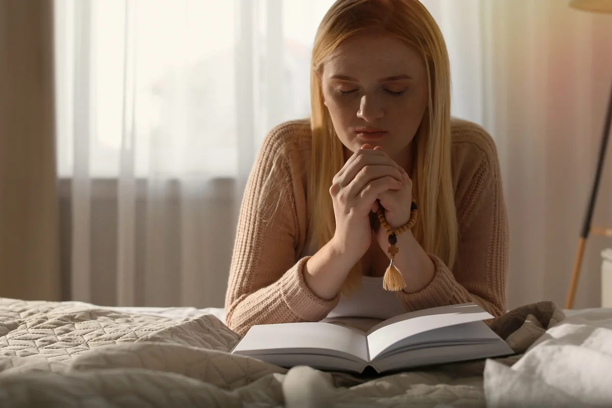 Young woman praying with folded hands over an open book, the stillness of Mary in Mary and Martha learning