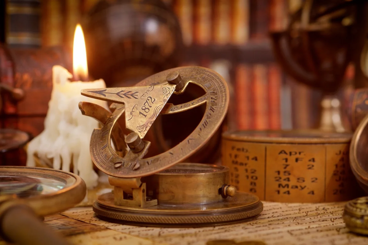Antique brass sundial and navigation instruments beside a candle and old books, tools of liberal arts and wisdom