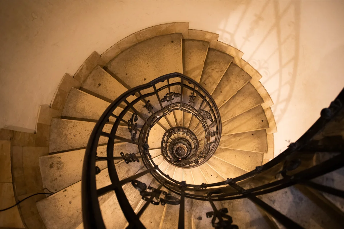 Stone spiral staircase with an iron railing winding upward toward the light, classical education for all students