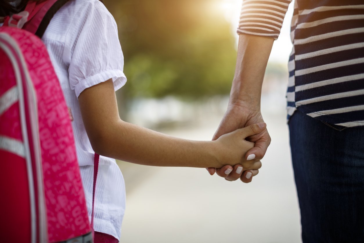 Child with a pink backpack holding a parent's hand on the way to school, asking if classical education is for everyone