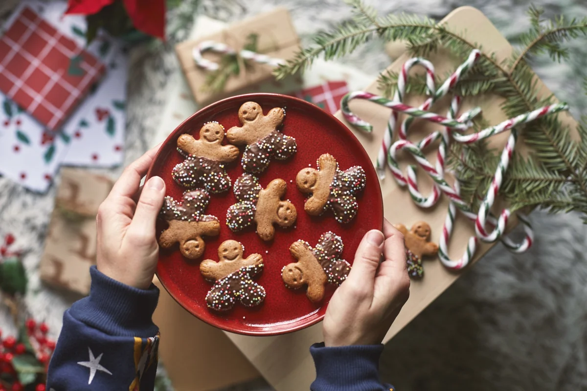 Hands holding out a red plate of gingerbread cookies to share, one of the Christian Christmas traditions for families