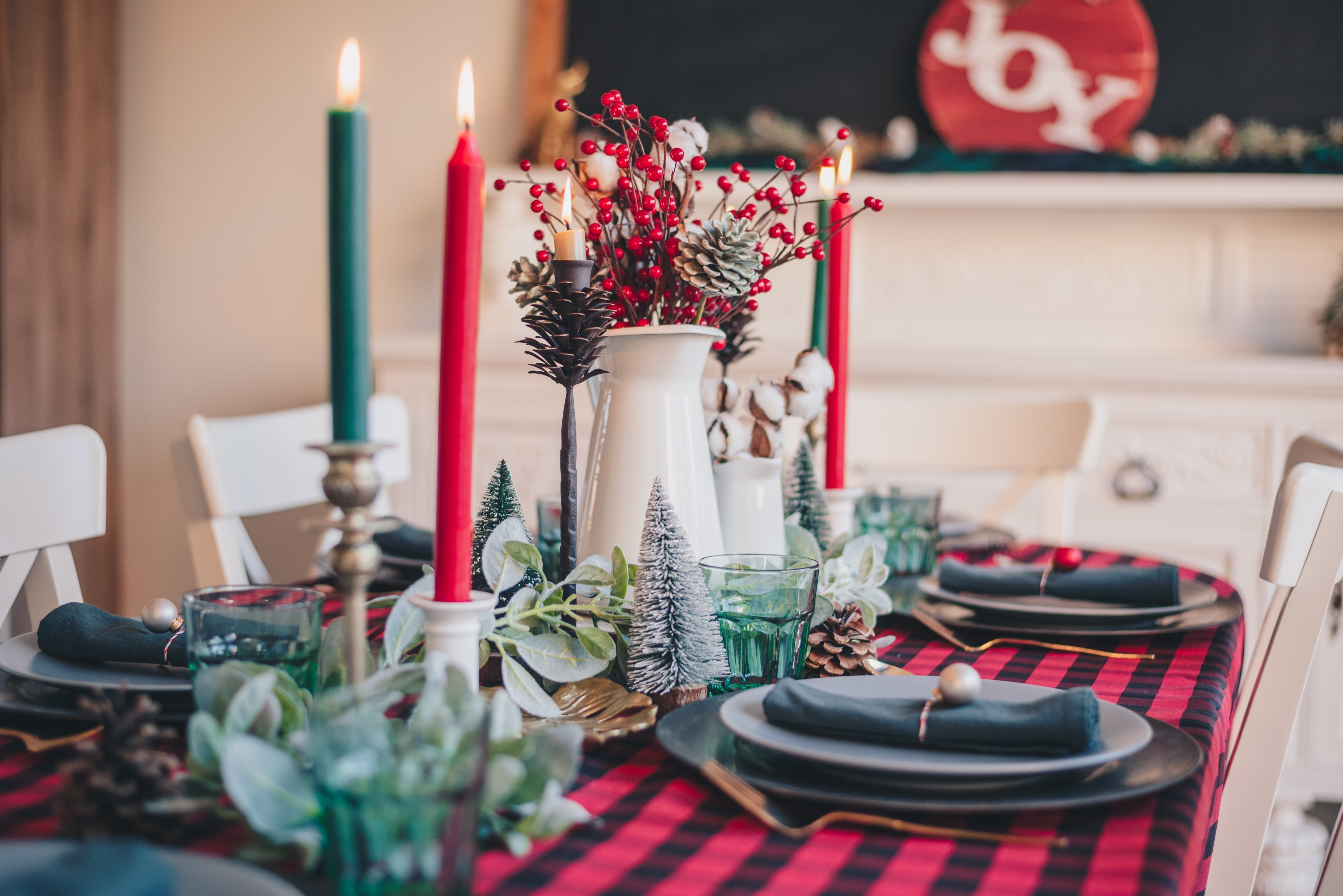 Christmas dinner table set with red and green candles, berries and plaid cloth, passing down Christmas traditions
