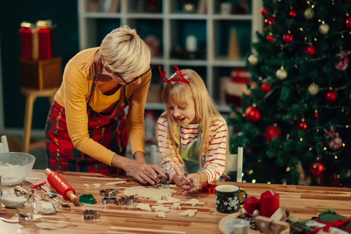 Grandmother and granddaughter cutting Christmas cookies at a kitchen table, keeping old Christmas traditions alive