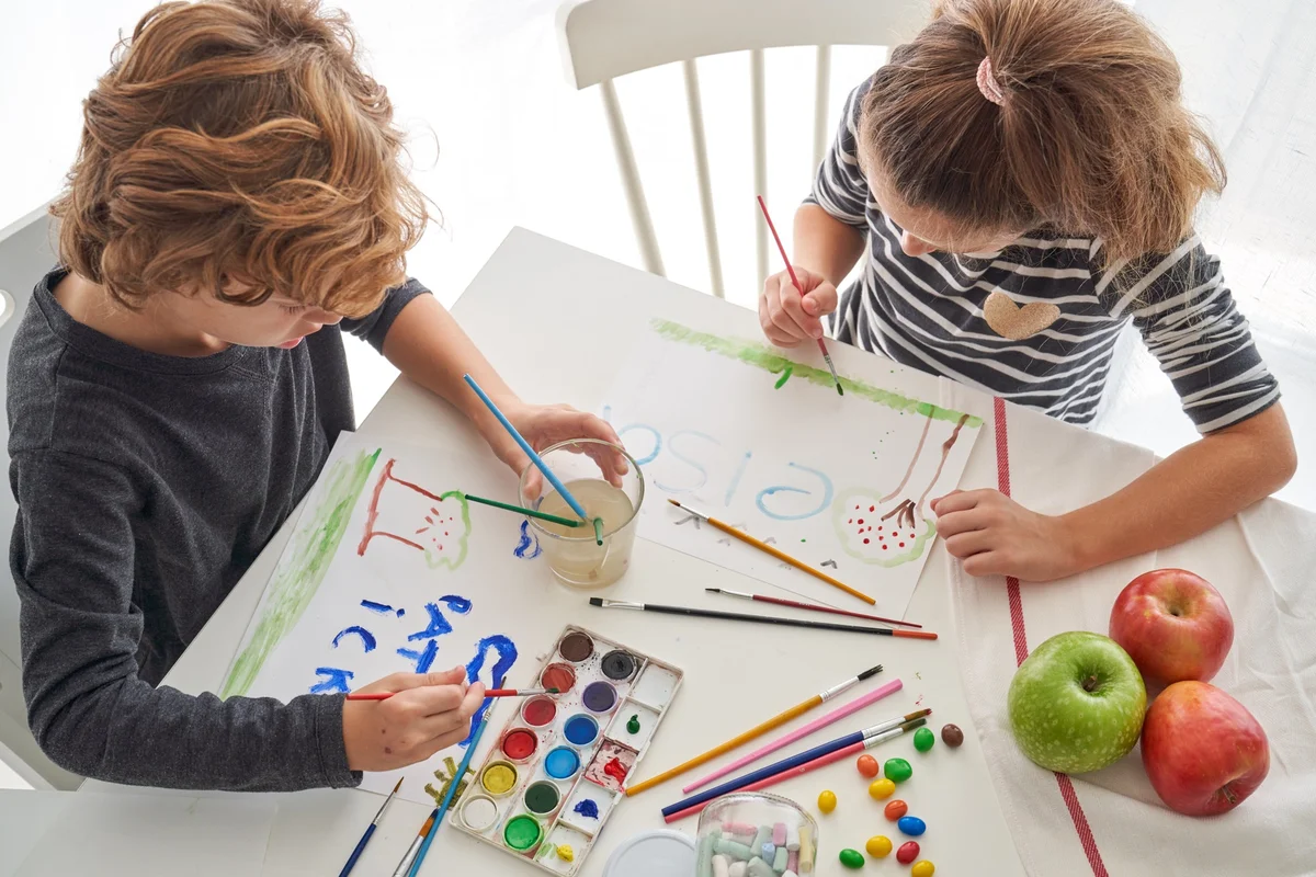 Two children painting with watercolors at a white table, one of the gentle liturgy classroom activities