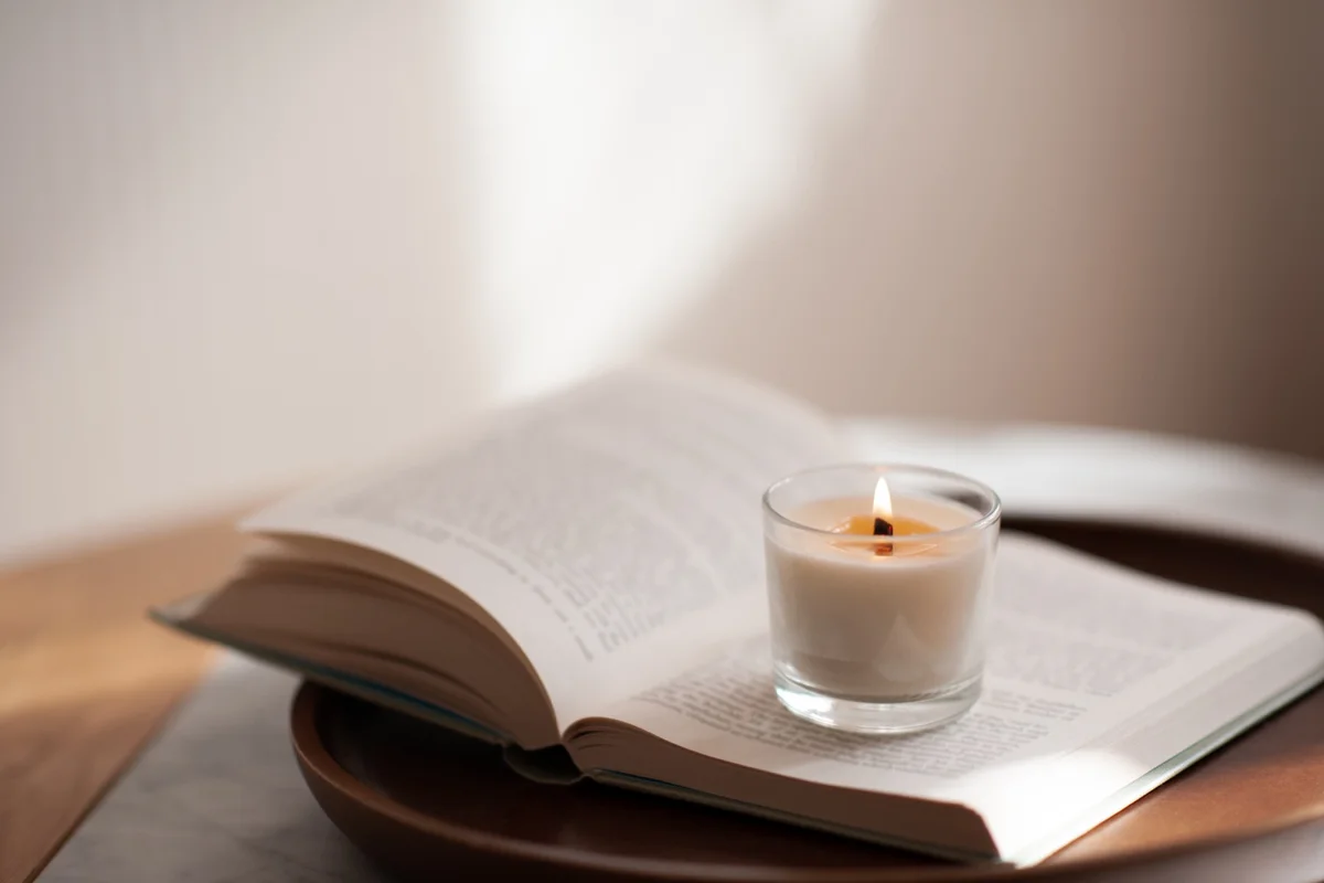 Lit candle resting on an open book in soft window light, a quiet liturgy for students and scholars before class