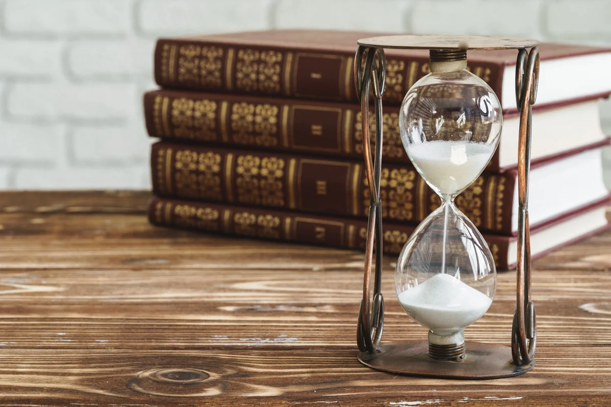 Hourglass with falling sand beside a stack of old leather books, weighing the time a school liturgy takes
