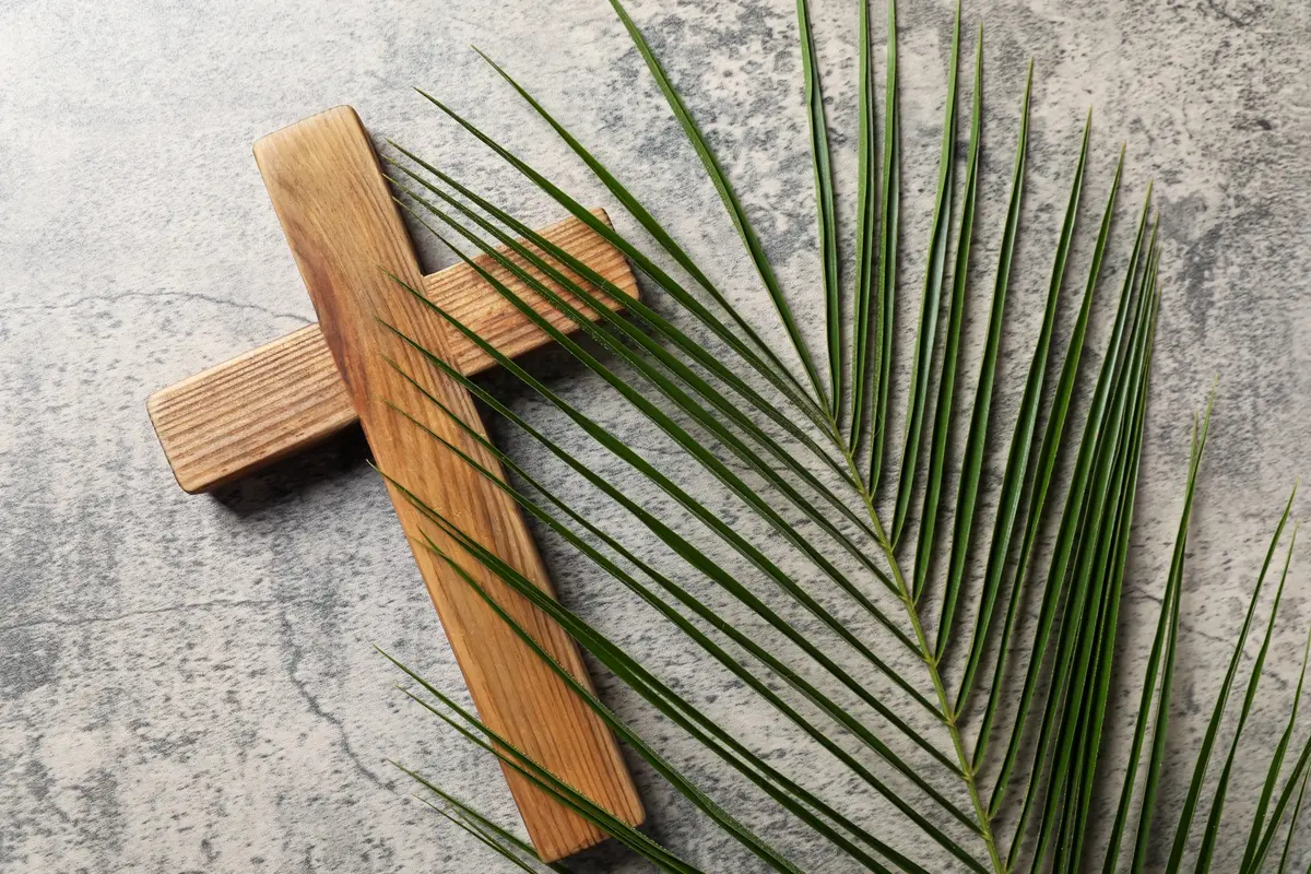 Wooden cross resting on a green palm frond on gray stone, the eve of Palm Sunday kept as Lazarus Saturday