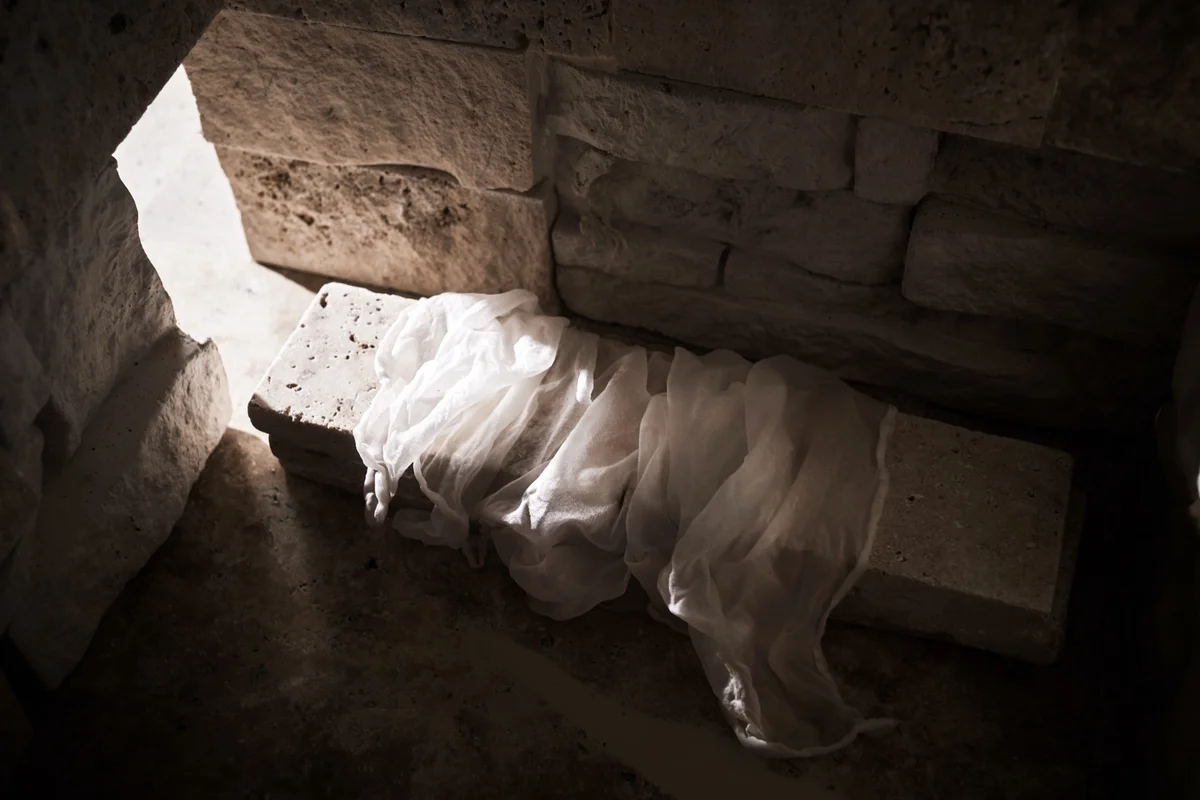 Light falling into an empty rock-cut tomb onto discarded white linen, recalling the raising of Lazarus and Christ's own