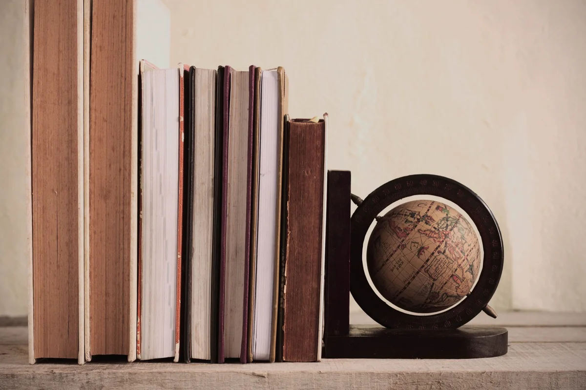 Row of old books held upright by a small globe bookend on a wooden shelf, the start of a year of fortitude