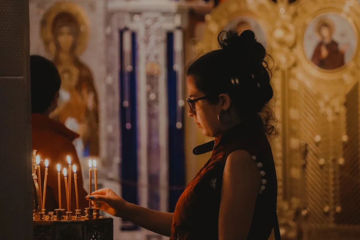 Young woman lighting beeswax candles before golden icons, the daily piety of raising children in the Orthodox faith