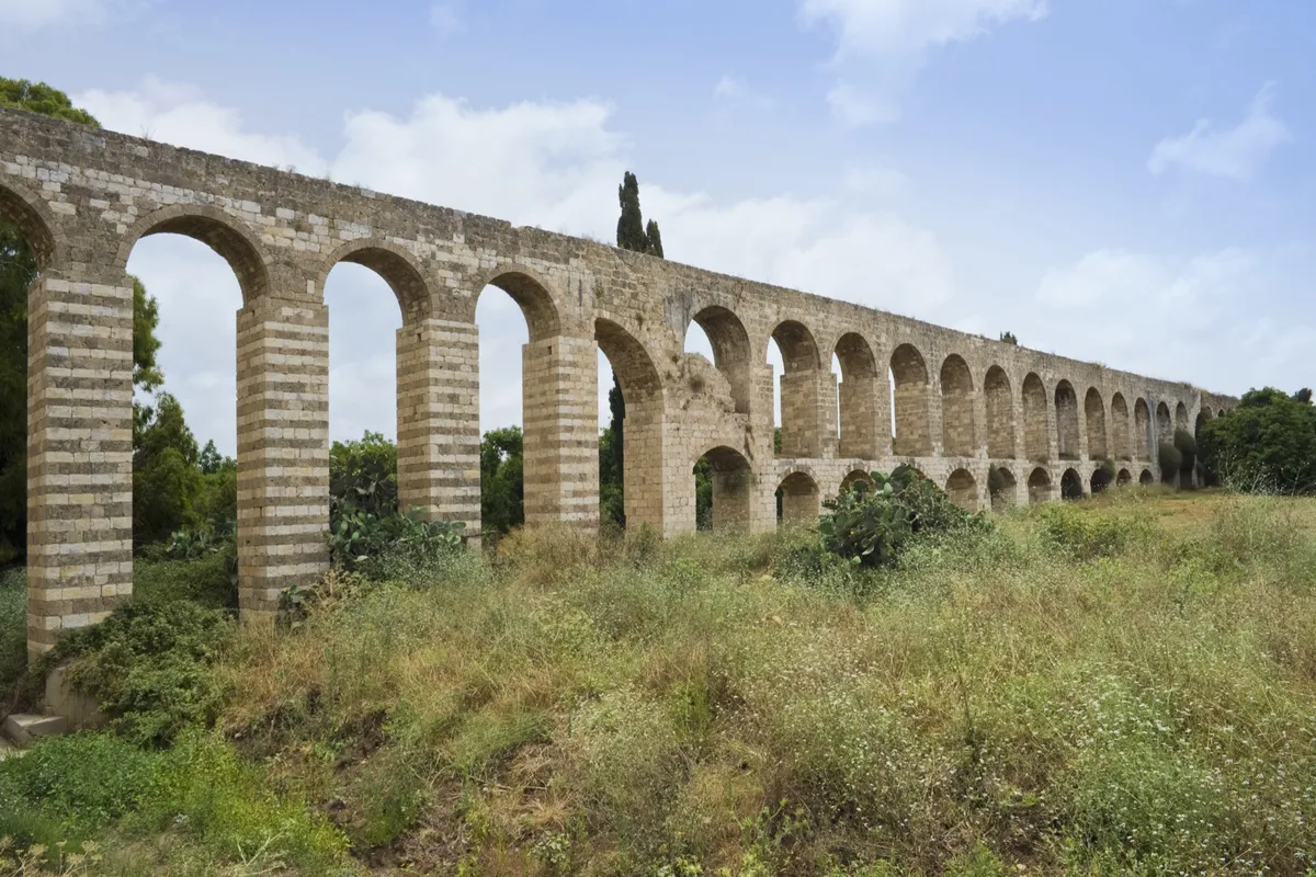 Long Roman aqueduct of matching stone arches across a green hillside, unified because each arch is ordered to the next