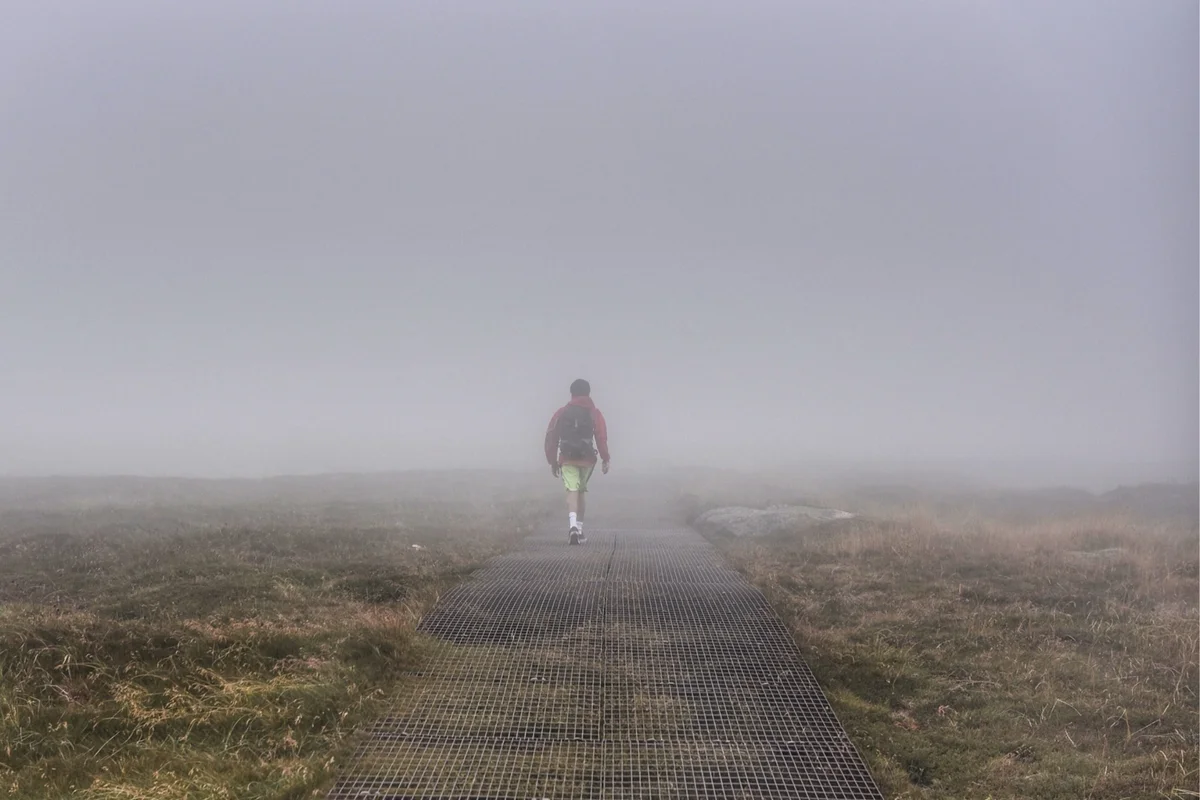 Lone figure walking a boardwalk path into thick fog across open moorland, a picture of Jane Eyre's virtue of temperance