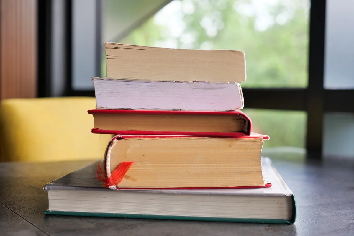 Stack of well-read hardcover books on a desk by a sunny window, a pile of worthy kids' books ready to share