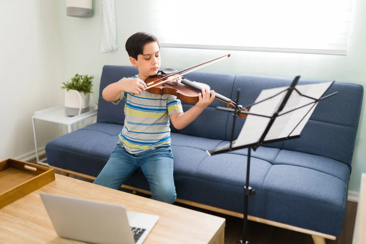 Boy practicing violin at a music stand in a bright living room, a first step into classical Christian music