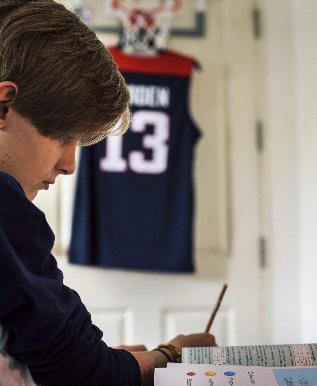 A boy in a jersey concentrating on his schoolwork