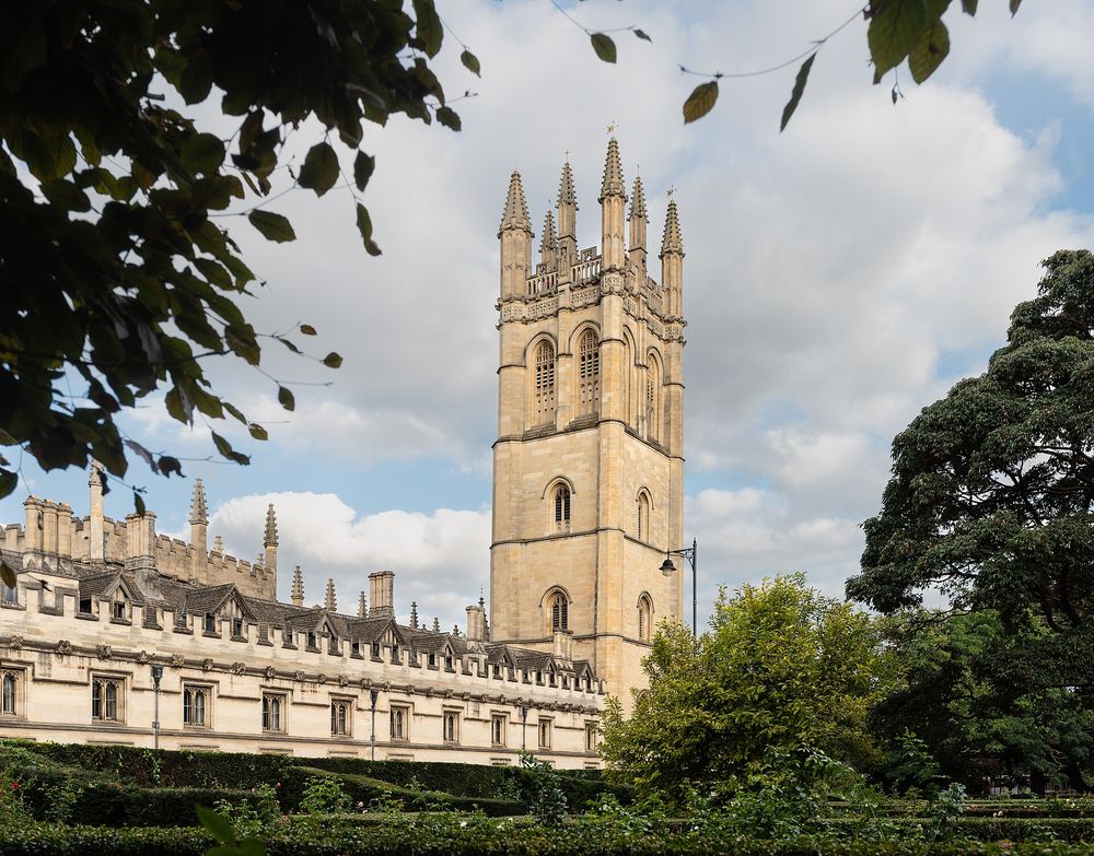 Magdalen Tower rising above the long stone range of Magdalen College, Oxford, framed by trees