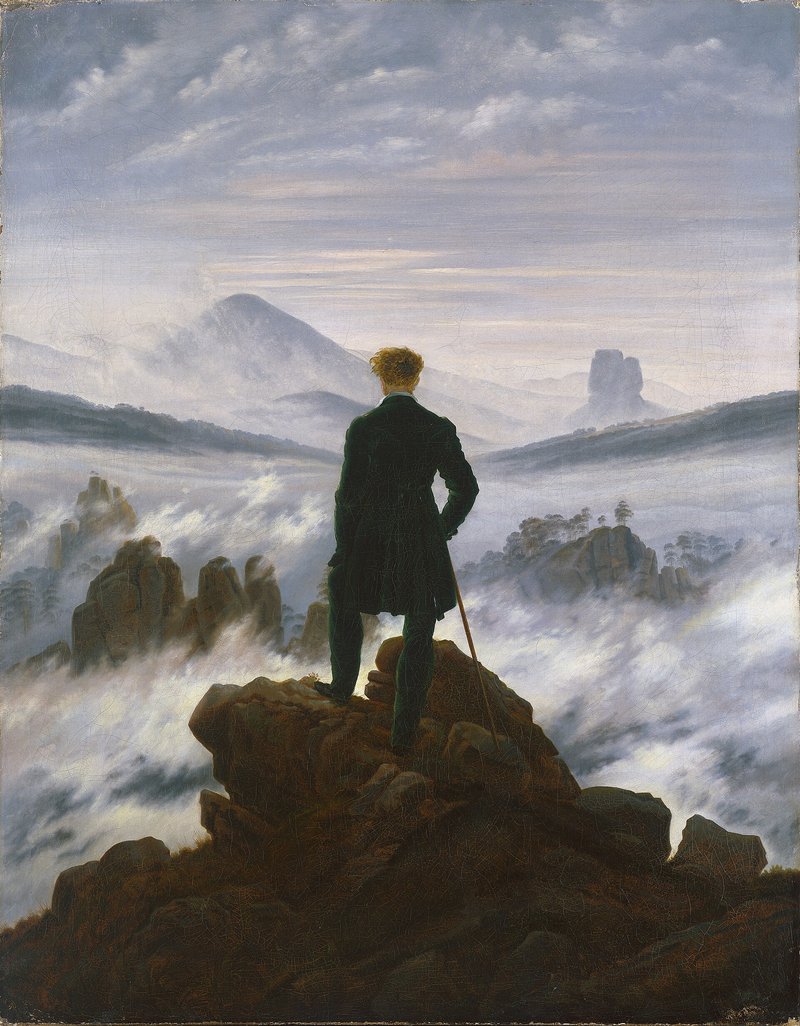 A man in a dark coat stands on a rocky summit, his back to the viewer, gazing over a sea of fog and distant peaks